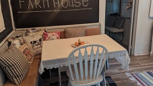A cozy seating area with a chalkboard sign reading "WELCOME TO THE FARM HOUSE," a table with a white tablecloth, and a chair with a white frame.