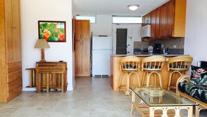 Una cocina compacta con armarios de madera, un refrigerador, una mesa de comedor con sillas y una pequeña isla con encimera de vidrio.