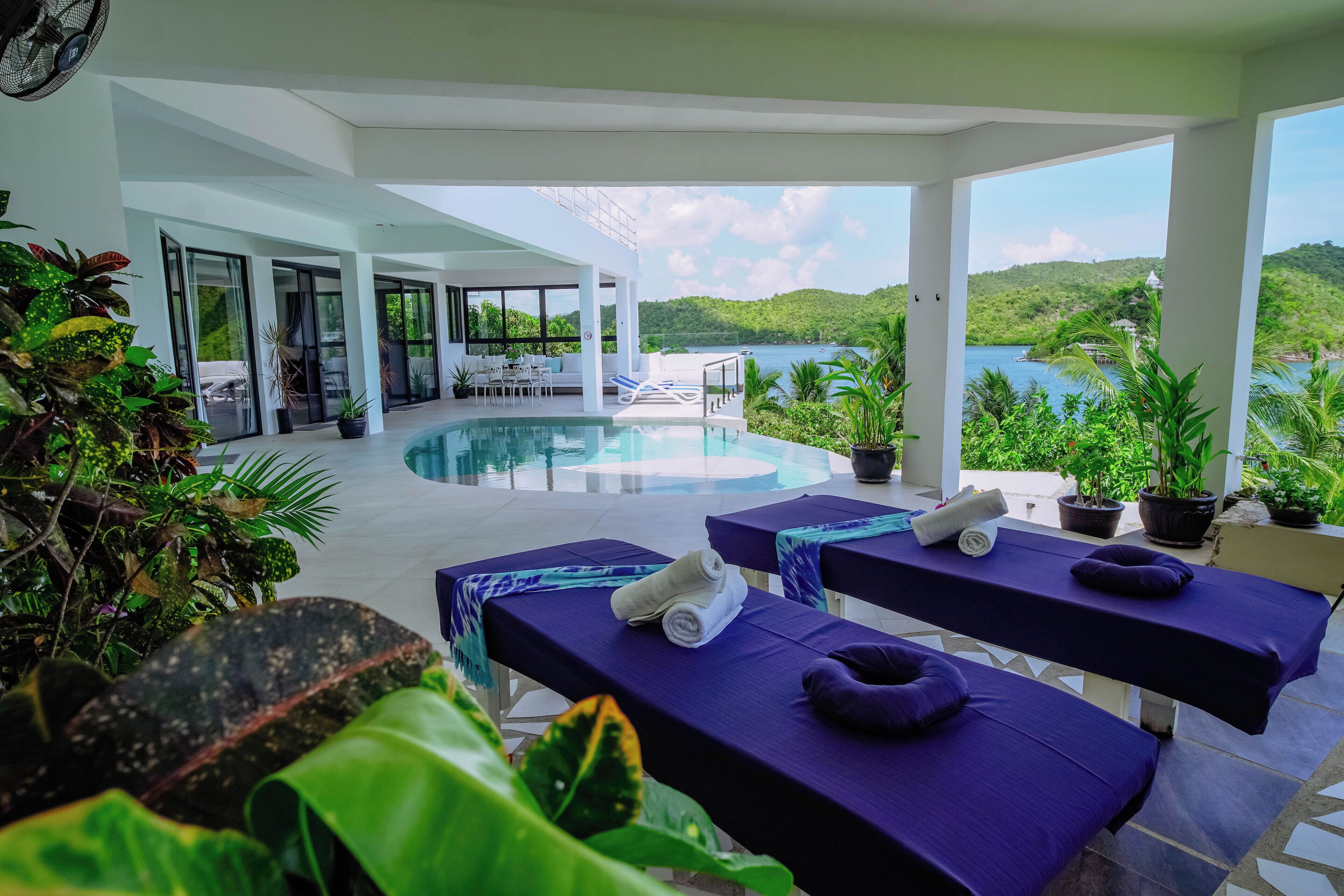 Zona junto a la piscina con dos camillas de masaje, una piscina y vistas a un lago y colinas.
