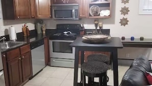Una cocina con armarios de madera, microondas, horno, lavaplatos y una mesa de comedor con dos sillas.