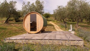Una struttura a botte in legno con una porta aperta, posizionata su un pontile di legno circondato da campi di lavanda e ulivi.