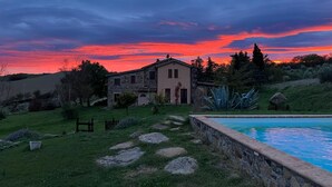 Una casa con facciata in pietra, piscina e giardino con rocce e piante.