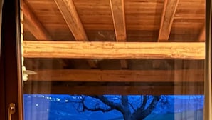 Una stanza con una grande finestra, travi in legno a soffitto e vista su un albero e un paesaggio.