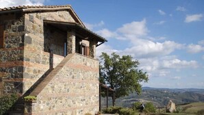 Un edificio in pietra con una scala che conduce a un portico coperto, immerso nel verde e con una vista panoramica sulle colline.