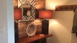 Um banheiro moderno com parede de detalhes em madeira, espelho, duas luminárias na parede, cesta trançada e um banco.