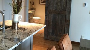 Cozinha com bancadas de granito, luminária pendente e porta de estilo rústico deslizante que dá para um banheiro.