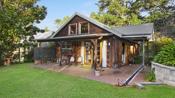 Ein Holzhaus mit überdachter Terrasse, einem umzäunten Garten und einem gepflegten Rasen.