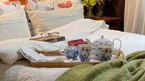 A neatly made bed with white linens, a tray with tea set, and a book titled "THE LAVENDER".