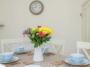 Une table à manger ornée d’un vase blanc rempli de fleurs, de bols aux motifs bleus et blancs, et d’une horloge accrochée au mur.