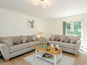 A living room with two sofas, a coffee table, a lamp, and a window with a view of greenery. - 3 bedroom accommodation in Fulletby, near Horncastle (Fulletby, near Horncastle)