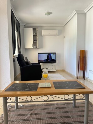 Un salon avec un téléviseur, un verre de jus d’orange et une table à manger avec deux sets de table.