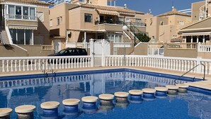 Una piscina con balaustra bianca, circondata da edifici beige con balconi e un cielo azzurro terso.