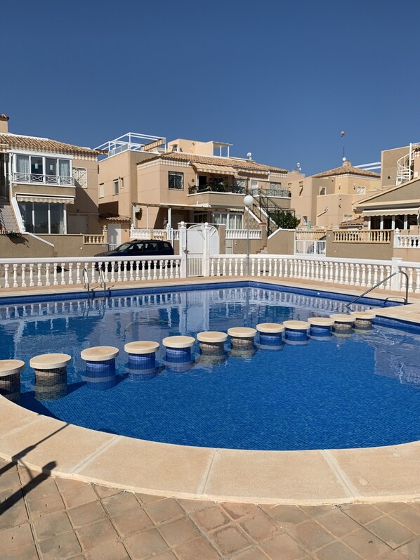 A swimming pool with a white balustrade, surrounded by beige buildings with balconies and a clear blue sky.