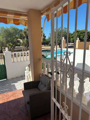 A covered outdoor seating area with a view of a swimming pool and greenery.