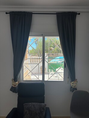 Une pièce avec une fenêtre, deux chaises et une vue sur un espace extérieur comprenant une piscine et de la verdure.