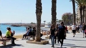 Una passeggiata con palme, panchine e persone che camminano.