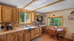 Una cocina con armarios de madera, una cafetera, un fregadero y un comedor con sillas y una mesa.