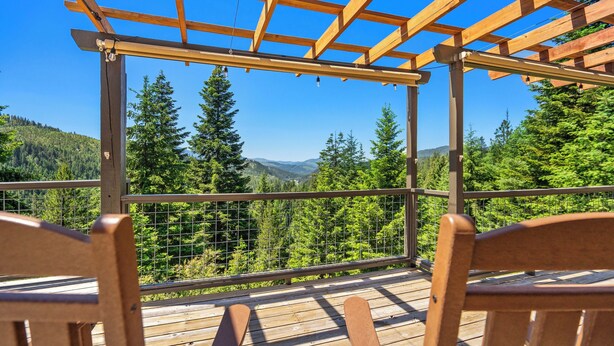 Una terraza de madera con pérgola, con vistas a un paisaje montañoso cubierto de bosque.