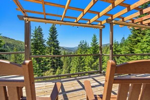 Una terraza de madera con pérgola, con vistas a un paisaje montañoso cubierto de bosque.
