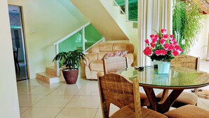 Una sala de estar moderna con una mesa de vidrio, sillas de mimbre, un sofá color beige y una planta en maceta.