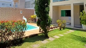 Una propiedad residencial con piscina, césped cuidado y un edificio de dos pisos con balcones.