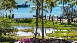 A tropical resort with a view of the ocean, palm trees, and a dock with a boat. - 3 BR penthouse with easy beach access - Hilton Waikoloa Access Included (Waikoloa)