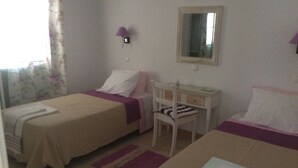 Hotellihuone, jossa on kaksi erillistä sänkyä, pieni työpöytä, tuoli ja peili seinällä.