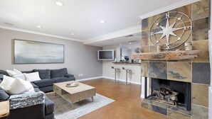 Una sala de estar moderna con un sofá gris oscuro, una mesa de centro de madera y una chimenea de piedra con una brújula decorativa.