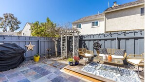 Un patio trasero con terraza, mobiliario exterior, una pérgola y una valla decorativa.