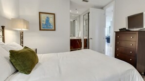 Ein Hotelzimmer mit einem Bett, einem Schminktisch, einem Fernseher und einem gerahmten Bild an der Wand.