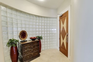 A corner room with a curved glass partition, a wooden cabinet with decorative items, and a wooden door with a geometric pattern.