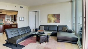 Ein modernes Wohnzimmer mit einem Ecksofa, einem Glastisch und einer Küche im Hintergrund.