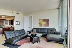 A modern living room with a sectional sofa, a glass coffee table, and a kitchen in the background. - Luxury 12th Floor Condo at Bella Luna (Orange Beach)