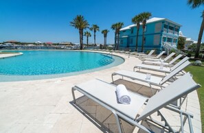 A pool area with lounge chairs and a blue building in the background. - Luxury 12th Floor Condo at Bella Luna (Orange Beach)