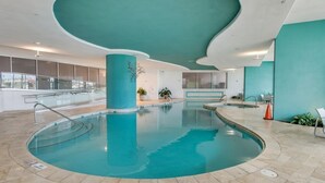 Una piscina interior con diseño curvo, rodeada por un suelo de baldosas y una pared color aguamarina.