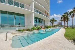 Un hotel moderno con piscina, balcón curvo y palmeras.