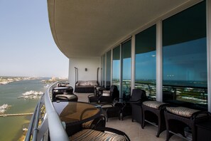 Enjoy the serene view of the water and cityscape from this balcony, featuring a comfortable wicker sofa, chairs, and table.