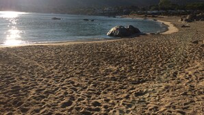 A beach with a rocky outcrop in the water, a clear sky, and mountains in the background.