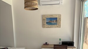A bedroom with a bed, a desk, a chair, a hanging light, an air conditioner, and a window.