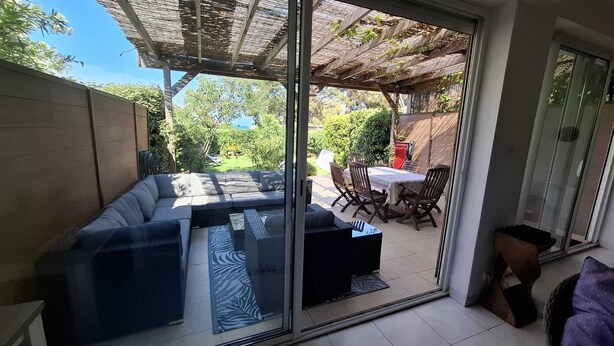 A modern living room with a sectional sofa, a dining table with chairs, and a pergola.