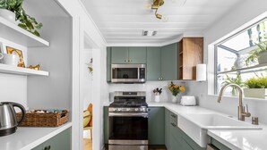 Una cocina compacta con microondas, estufa y lavabo, que presenta gabinetes verdes y encimeras blancas.