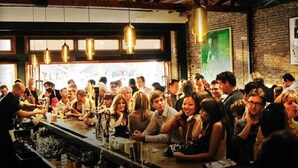 Un bar concurrido con vigas de madera y luces colgantes.