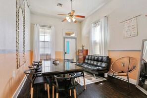 A room with a dining table, chairs, a sofa, a chair, a ceiling fan, and a door.
