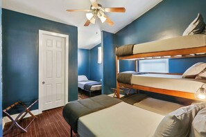 Ein kleines Zimmer mit Etagenbett, einem Einzelbett, Deckenventilator und einer Tür.