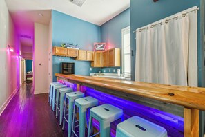 A bar area with stools, a wooden counter, and a neon sign.