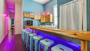 Un espace bar avec des tabourets, des meubles en bois et des enseignes au néon.