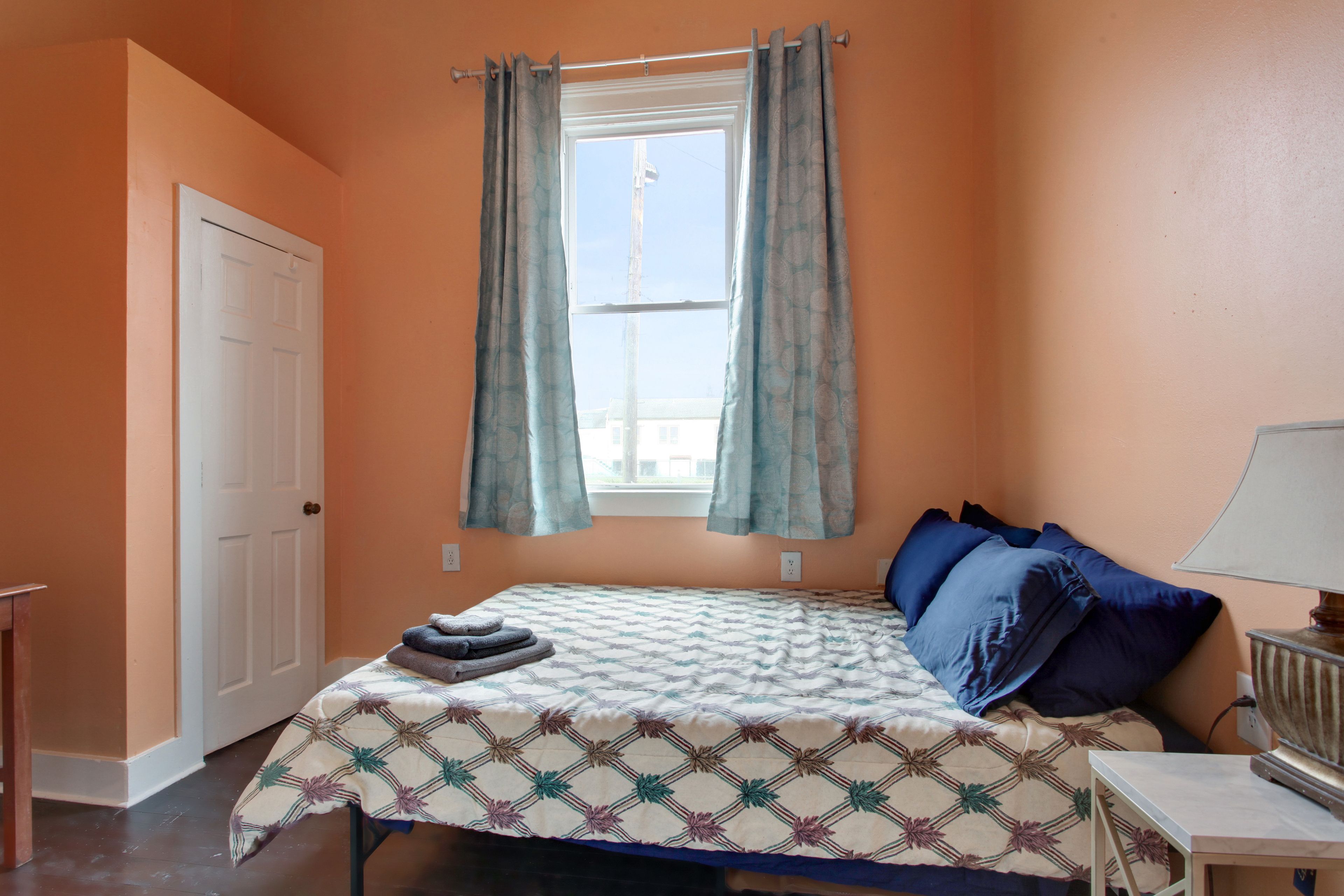 Une chambre à coucher avec un lit, une fenêtre avec des rideaux, une table de chevet avec une lampe et une porte.