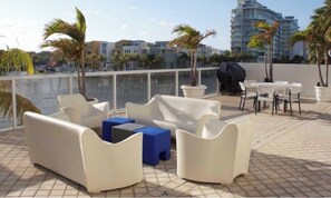 A rooftop terrace with white outdoor furniture, a grill, and a view of the city skyline.