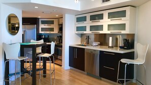 A modern kitchen with a dining area, featuring stainless steel appliances, white cabinetry, and a wooden floor. - Spectacular Views, Great Location on Millionaire's Row (Miami Beach)