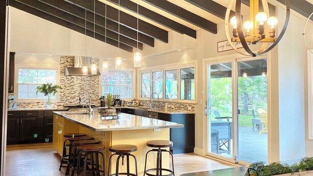 A modern kitchen with a large island, bar stools, pendant lighting, and a view of the outdoors.